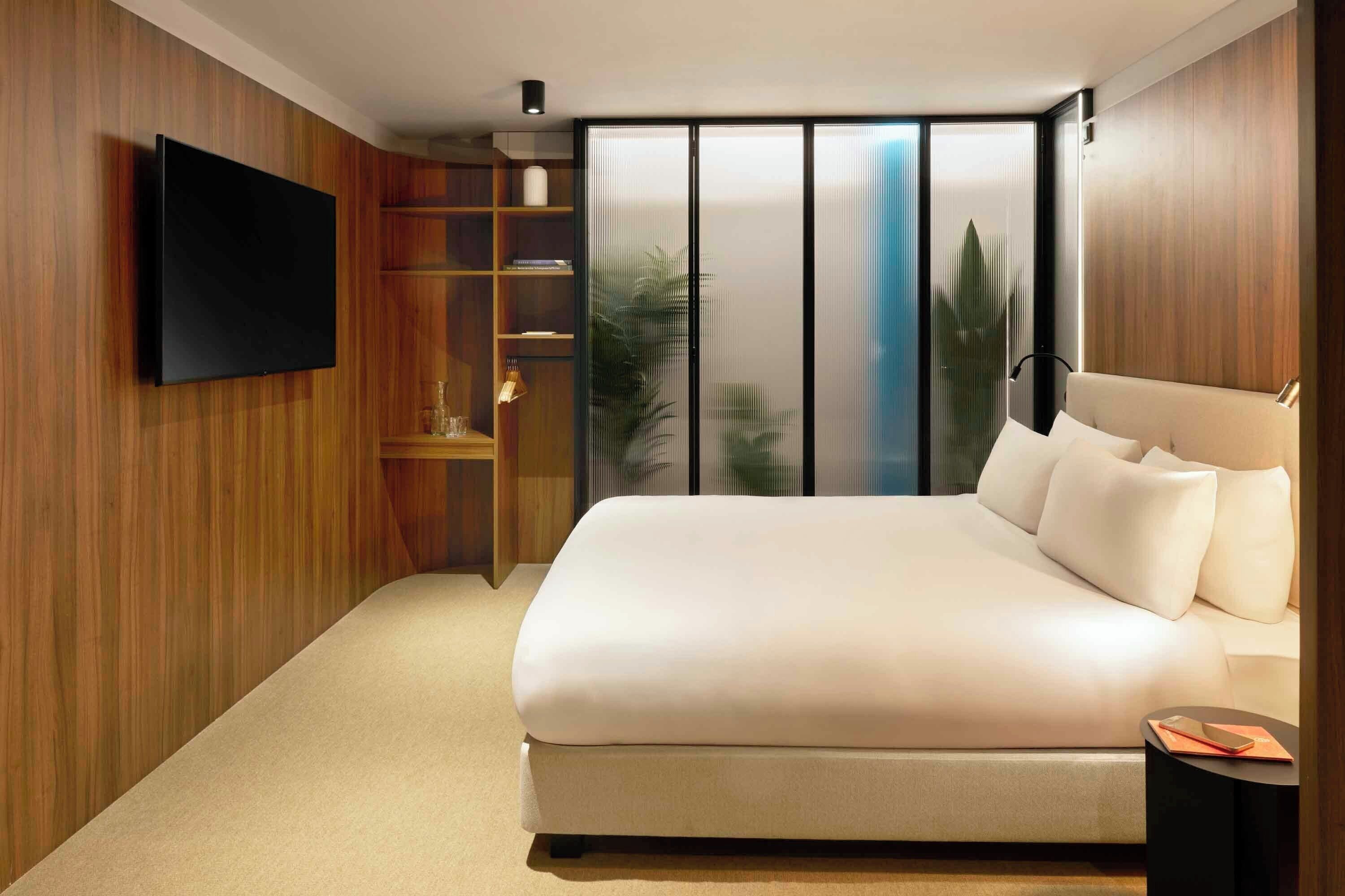 Una camera da letto moderna con un letto grande, una televisione a schermo piatto montata a parete e una porta vetrata scorrevole che dà su un balcone.