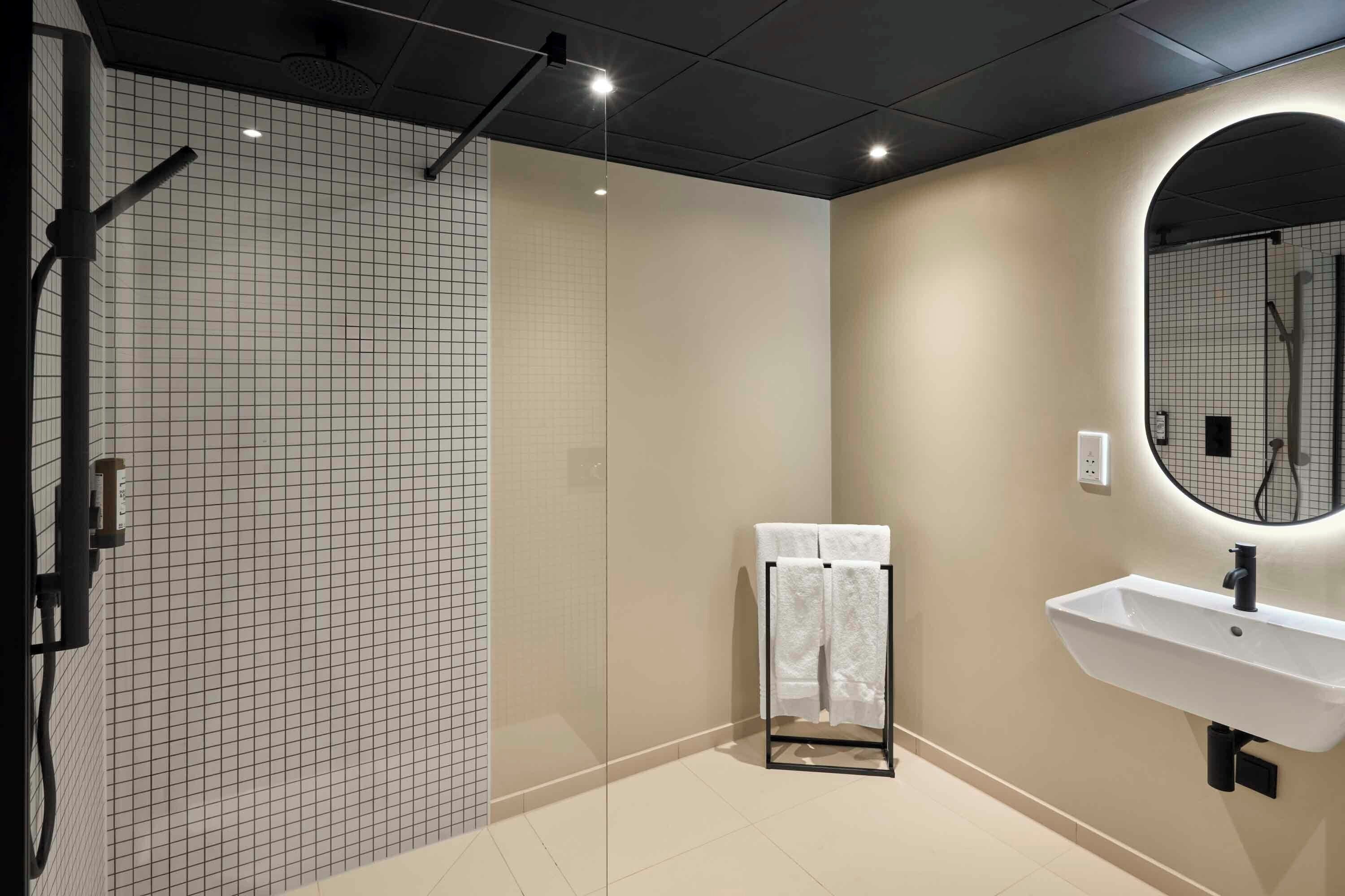 A modern bathroom with a glass shower enclosure, a white sink, and a mirror.