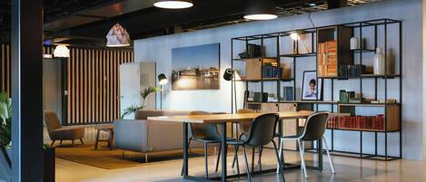 A modern office space with a wooden desk, chairs, a bookshelf, and a large window with blinds.