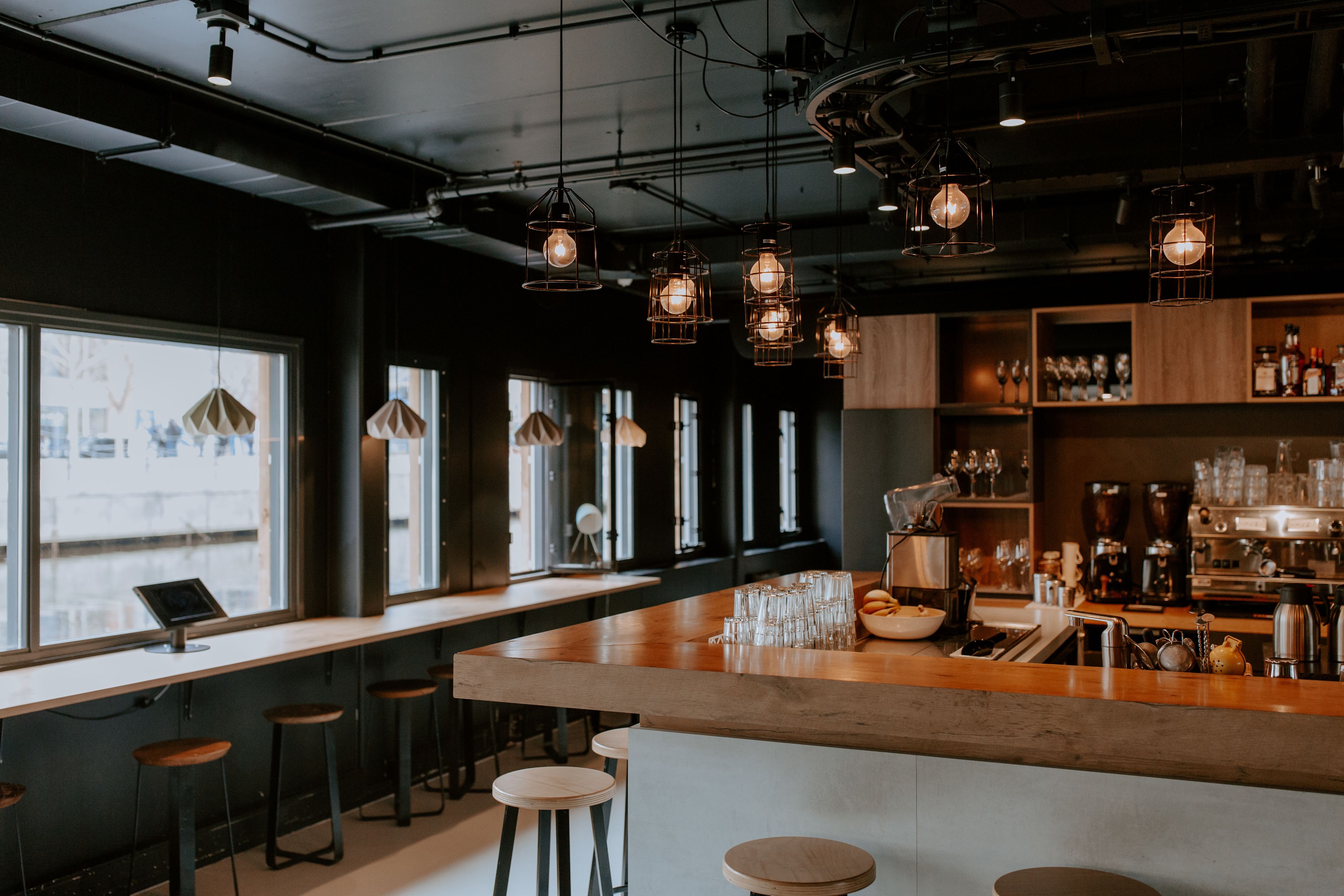 A bar area with stools, a counter with glasses, and a coffee machine.