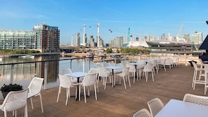 A rooftop terrace with tables and chairs overlooking a city skyline and a river. - Good Hotel London (London)
