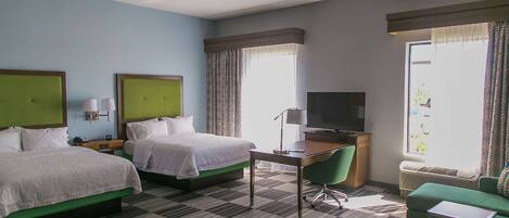 Quarto de hotel com duas camas, uma mesa, uma televisão e uma poltrona verde.