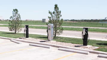 Un espace de stationnement équipé de bornes de recharge pour véhicules électriques, un ciel dégagé et une route en arrière-plan.