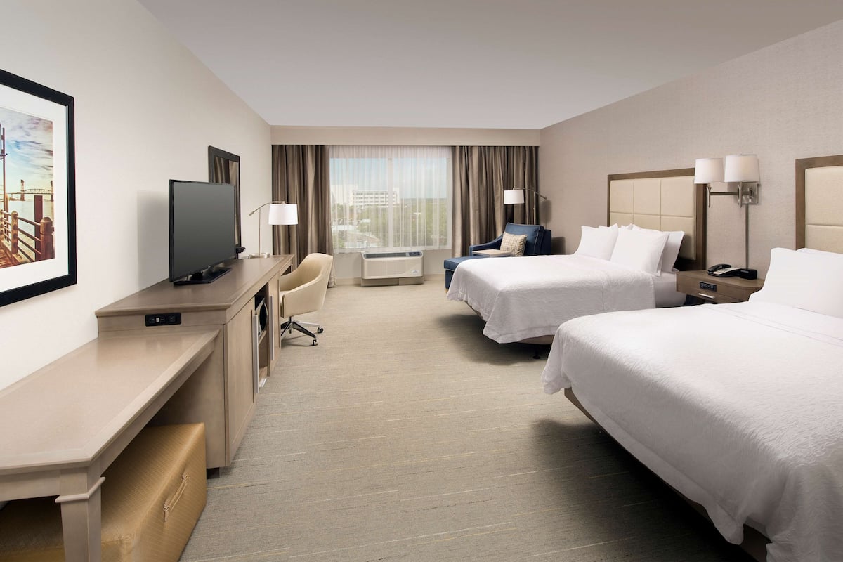 A hotel room with two beds, a desk with a TV, a chair, and a window with curtains.