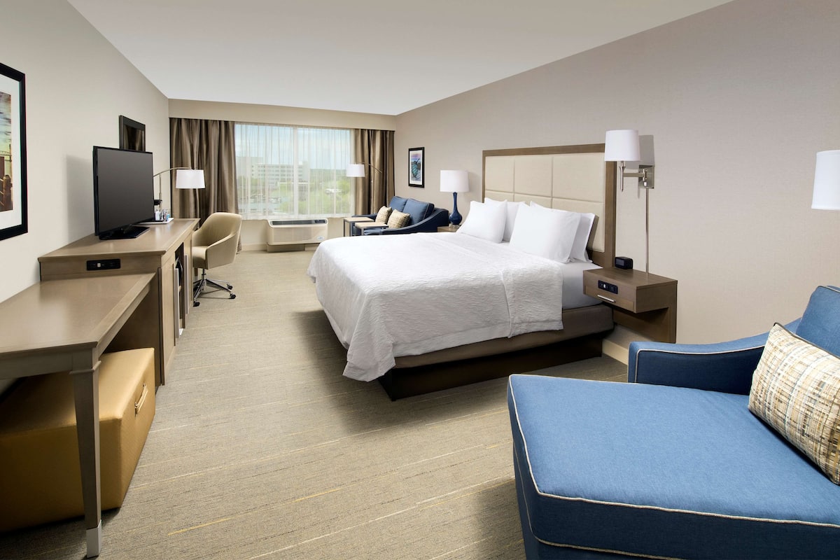 A hotel room with a bed, a desk, a chair, a TV, and a sofa.