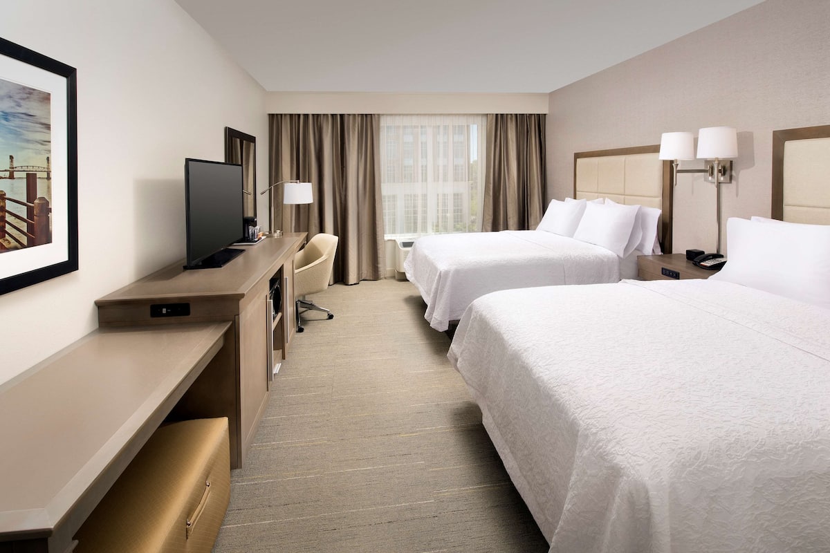 A hotel room with two beds, a desk with a TV, a chair, and a window with curtains.