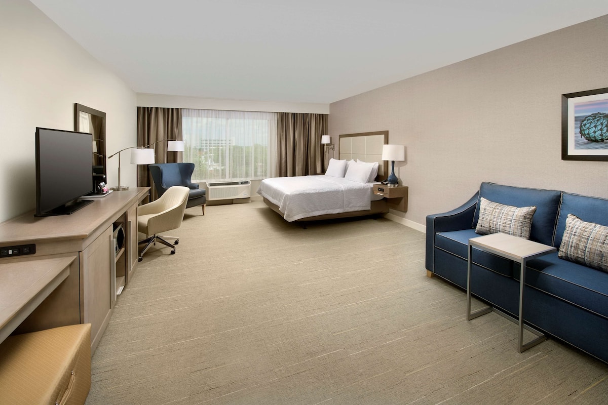 A hotel room with a bed, a desk with a computer, a chair, a blue sofa, and a TV.