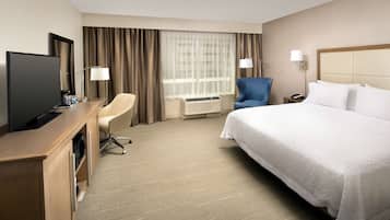 A hotel room with a bed, a desk with a television, a chair, and a window with curtains.