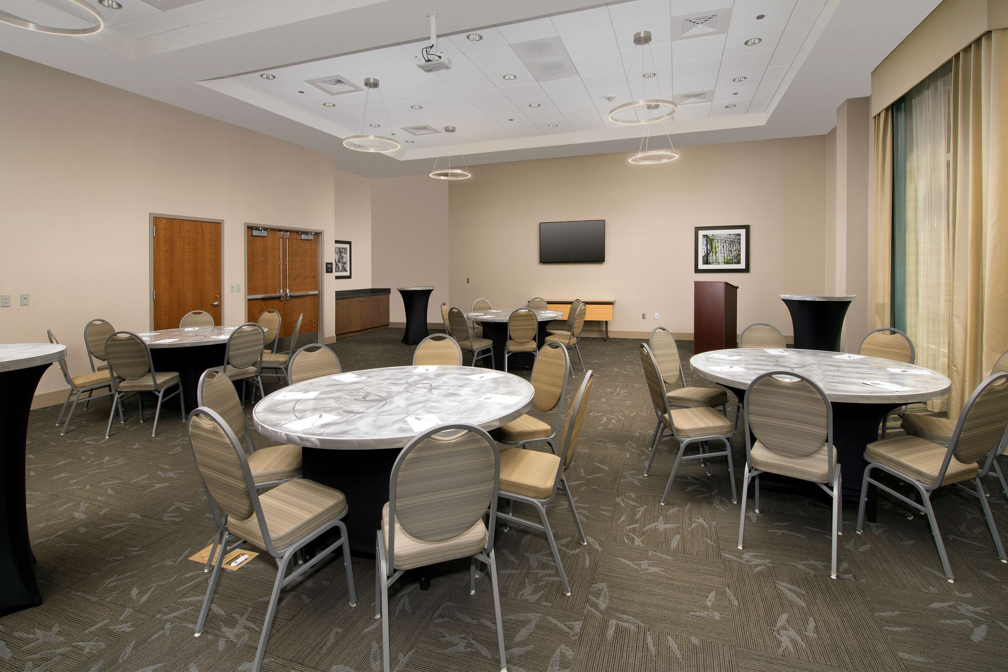 A conference room with round tables and chairs, a flat-screen TV, and a carpeted floor.