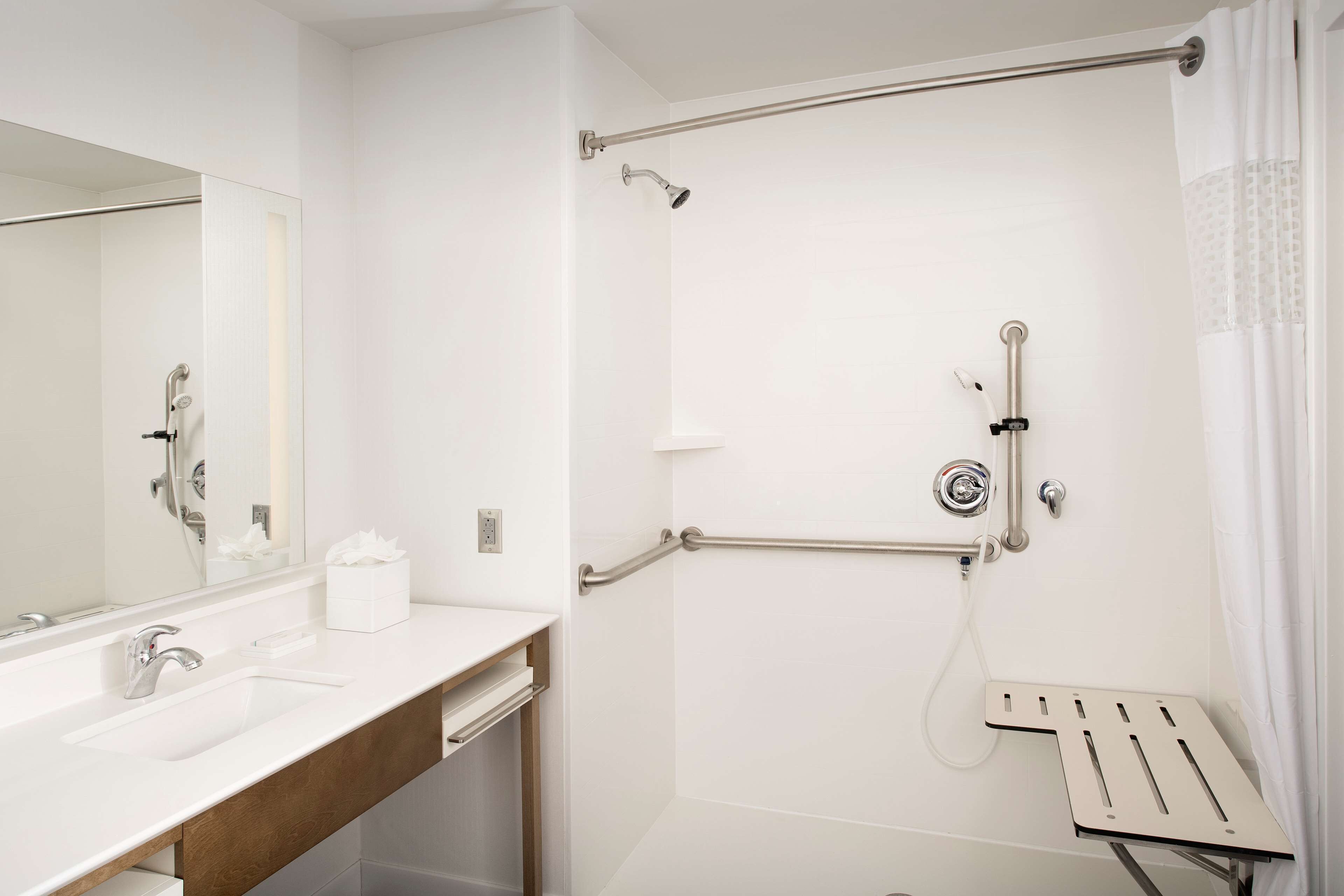 A modern bathroom with a white sink, a mirror, a shower with a grab bar, and a towel rack.