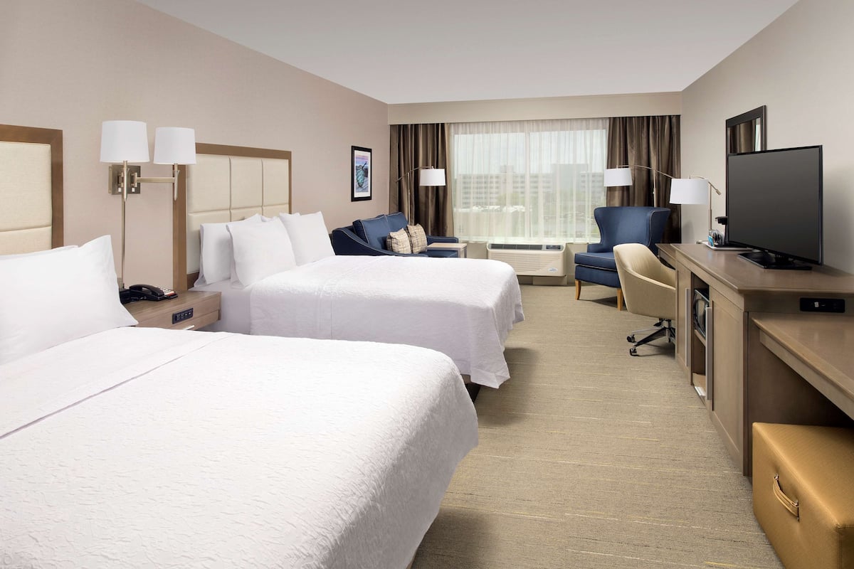 A hotel room with two beds, a desk, a chair, a television, and a window with curtains.