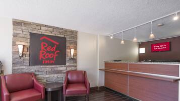 A Red Roof Inn reception area with a stone wall, two leather chairs, a wooden reception desk, and a sign indicating free Wi-Fi in all rooms.