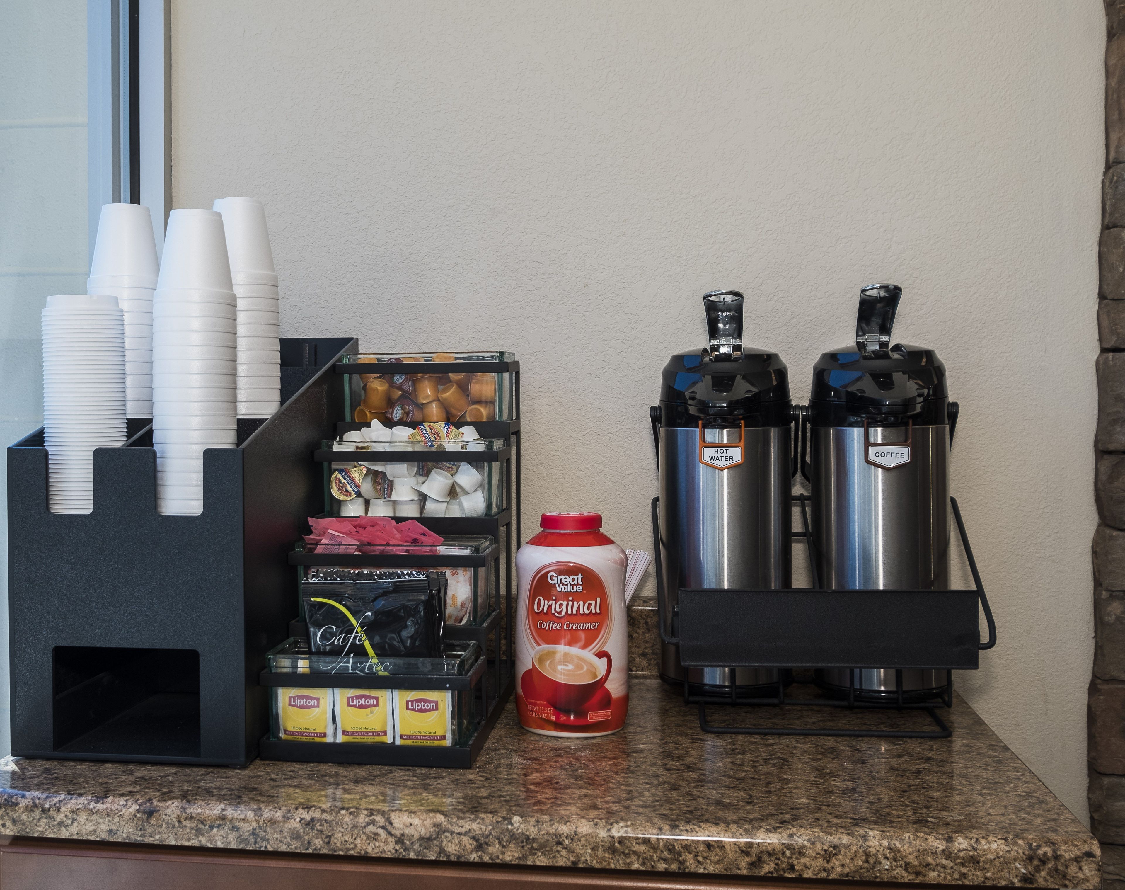 A coffee station with disposable cups, a coffee creamer dispenser, and two coffee dispensers.
