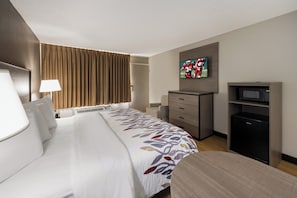 A hotel room with a large bed, a desk, a television, and a minibar.