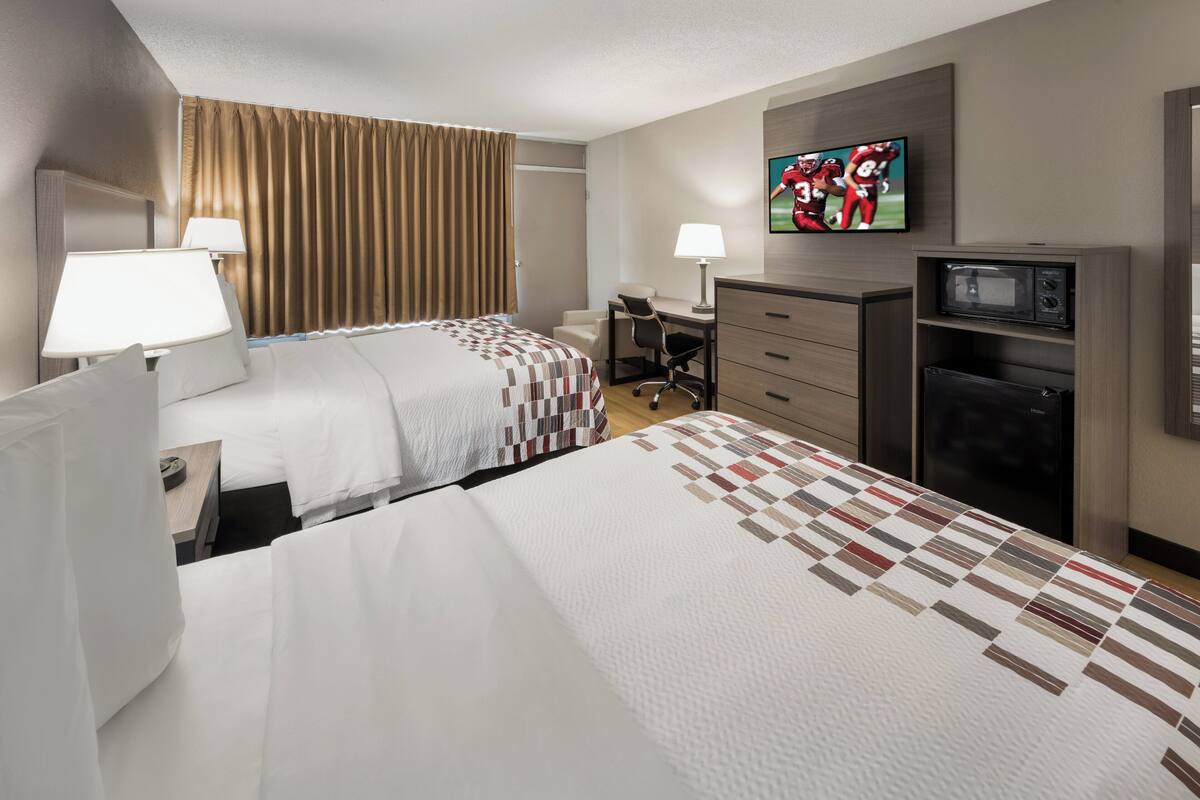 Une chambre d’hôtel avec deux lits, un bureau, une chaise, une télévision et un four à micro-ondes.