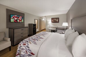 Een hotelkamer met een bed, een aan de muur bevestigde televisie, een bureau, een stoel, een dressoir en een deur.