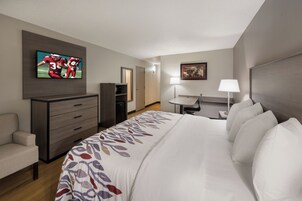 Habitación de hotel con cama, televisión montada en la pared, escritorio, silla, cómoda y puerta.