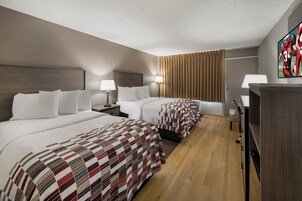 Una habitación de hotel con dos camas, un televisor, un escritorio y un armario.