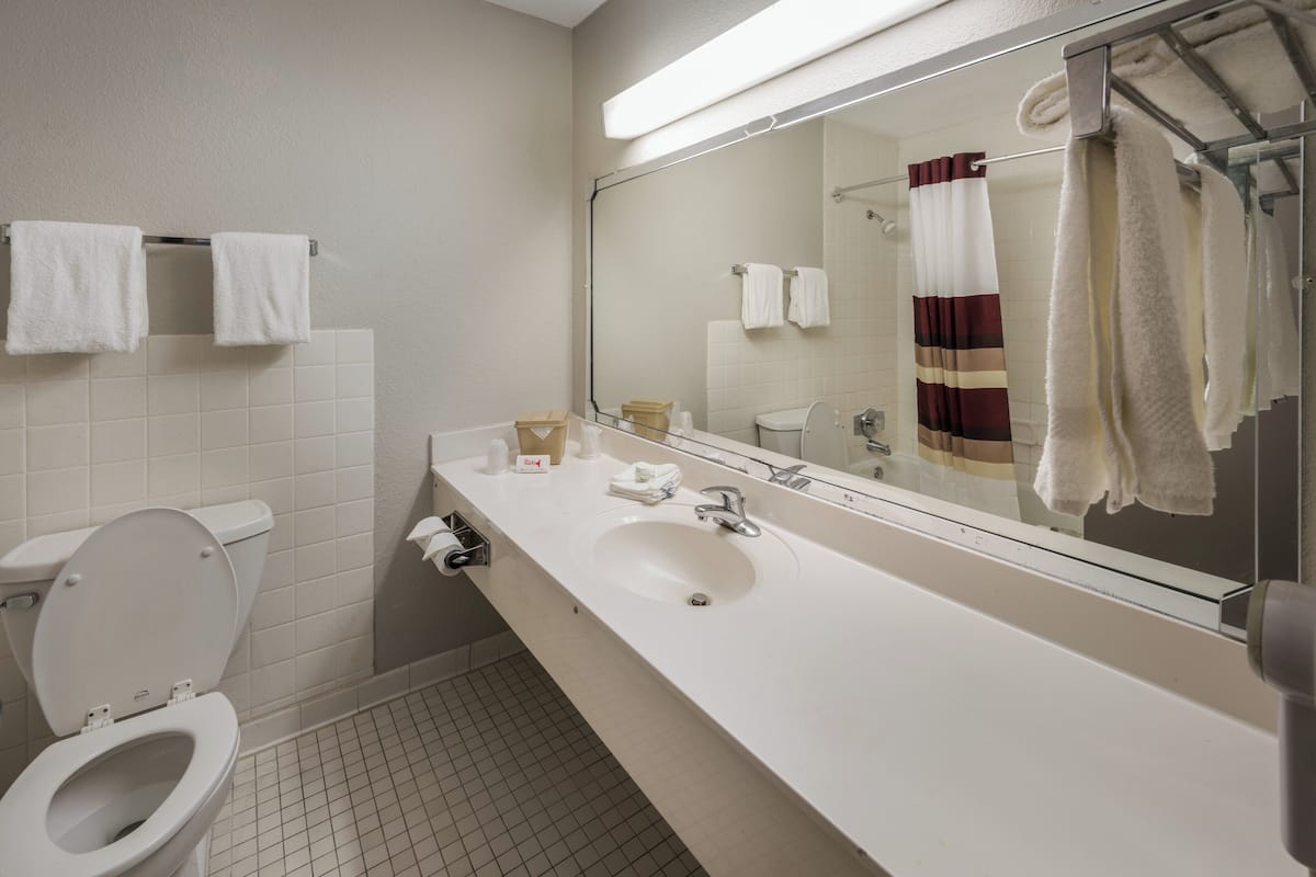 A bathroom with a white sink, mirror, and toilet. There are towels hanging on the wall and a shower curtain.