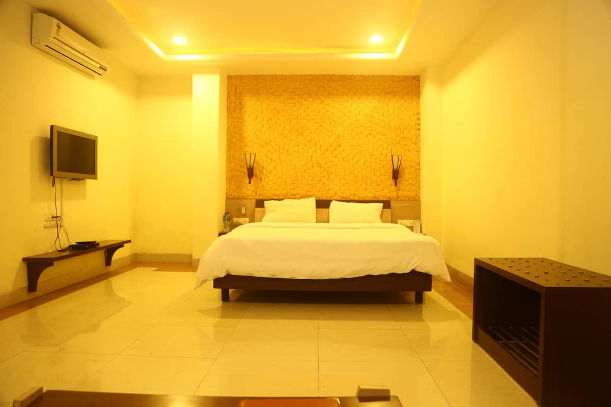 A hotel room with a large bed, a flat-screen TV mounted on the wall, a small table, and a wall-mounted air conditioner.