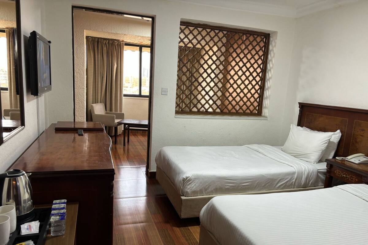 A hotel room with two beds, a desk with a coffee maker, a TV, and a window with a lattice screen.