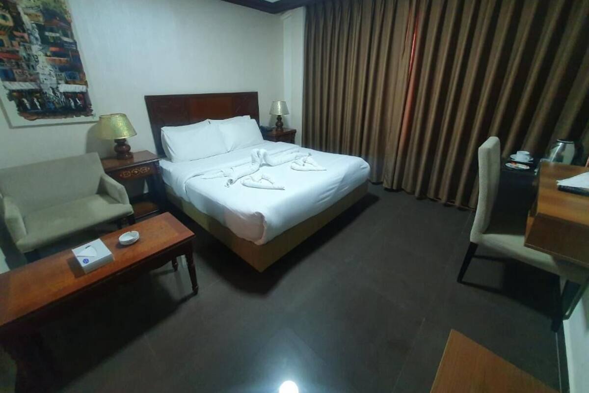 A hotel room with a bed, a desk, a chair, a nightstand, and a lamp.