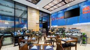 Een modern restaurant met meerdere eettafels, stoelen en een zichtbare keuken achter glazen wanden.
