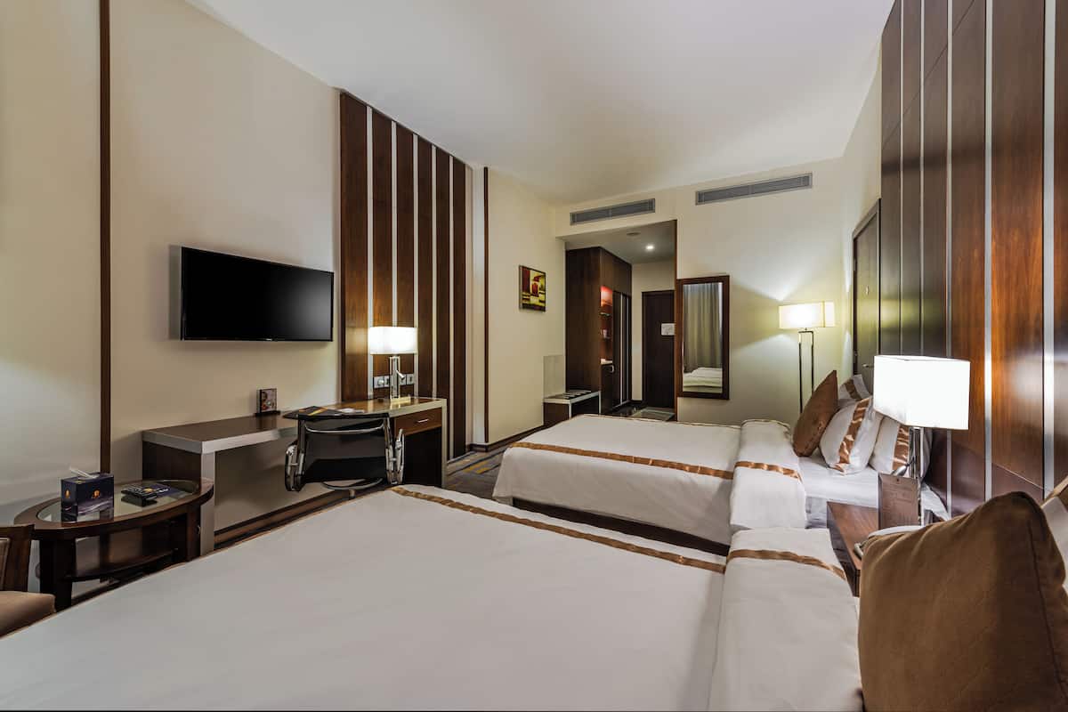 Une chambre d’hôtel avec deux lits, un bureau avec une chaise, un téléviseur à écran plat fixé au mur et une petite table avec une lampe.