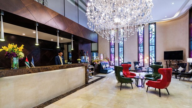 Een hotel lobby met een receptiebalie, een kroonluchter, een zithoek en grote ramen.
