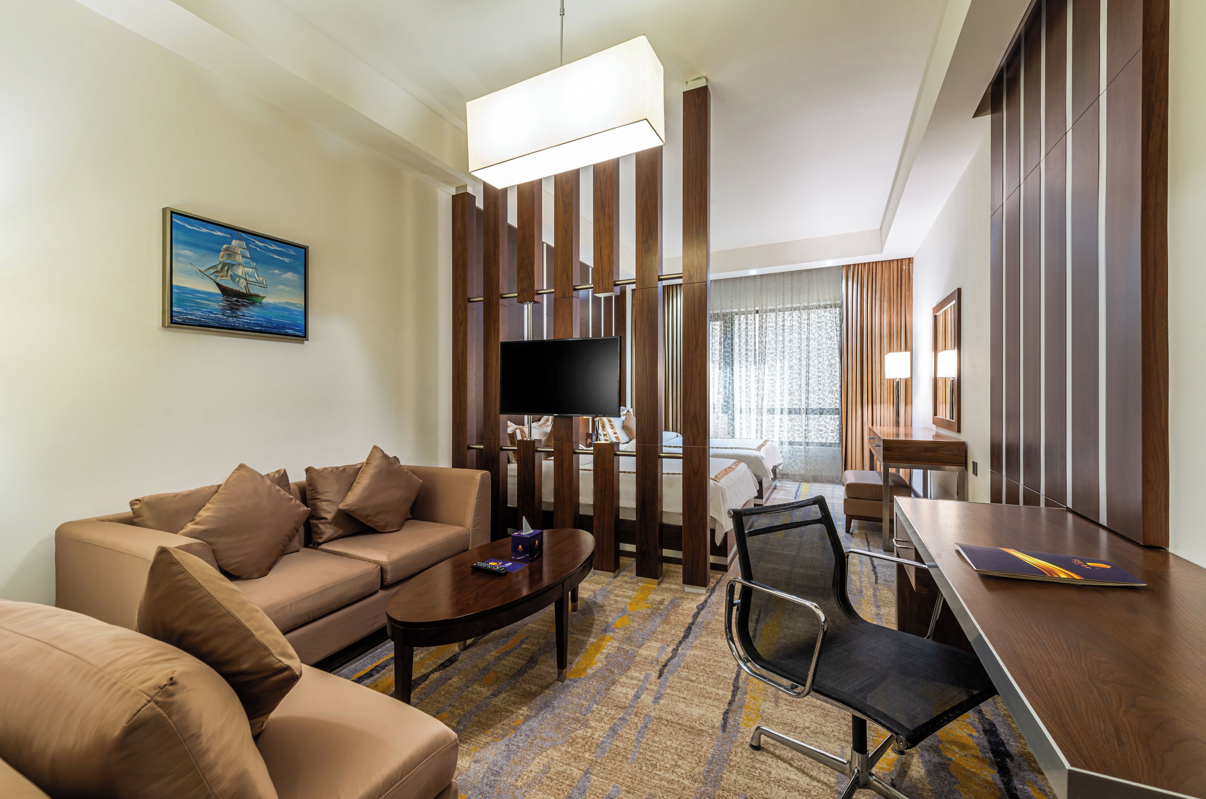 Una habitación de hotel moderna con sofá, mesa de centro, televisor, escritorio y un ventanal grande.