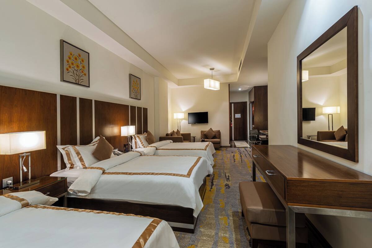 Une chambre d’hôtel avec trois lits, un bureau, une chaise, une télévision et un grand miroir.