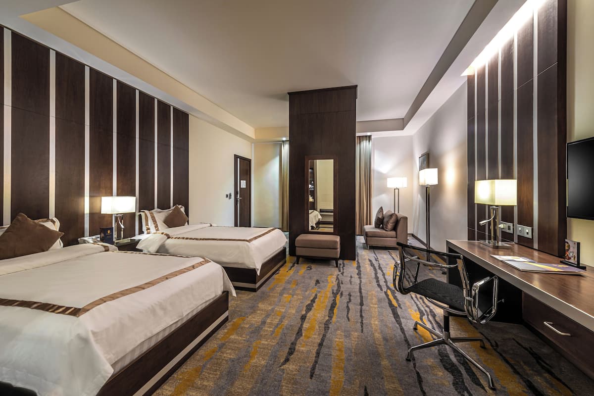 Une chambre d’hôtel avec deux lits, un bureau, une chaise, une télévision et un grand miroir.
