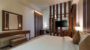 Een hotelkamer met een groot bed, een bureau met stoel, een spiegel, een televisie en een kledingkast.