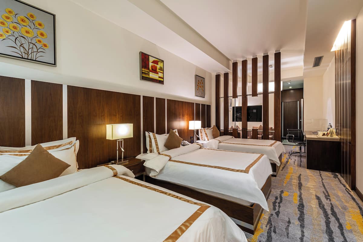 Une chambre d’hôtel avec trois lits, des têtes de lit en bois, un bureau et une chaise.
