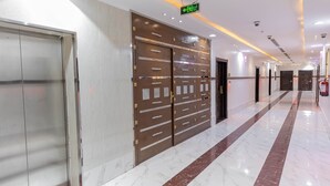 A hotel corridor with a marble floor, double doors with a security panel, and a fire extinguisher on the wall.