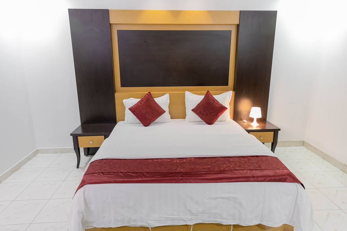 A hotel room with a large bed, two nightstands, a bedside lamp, and a wooden headboard.