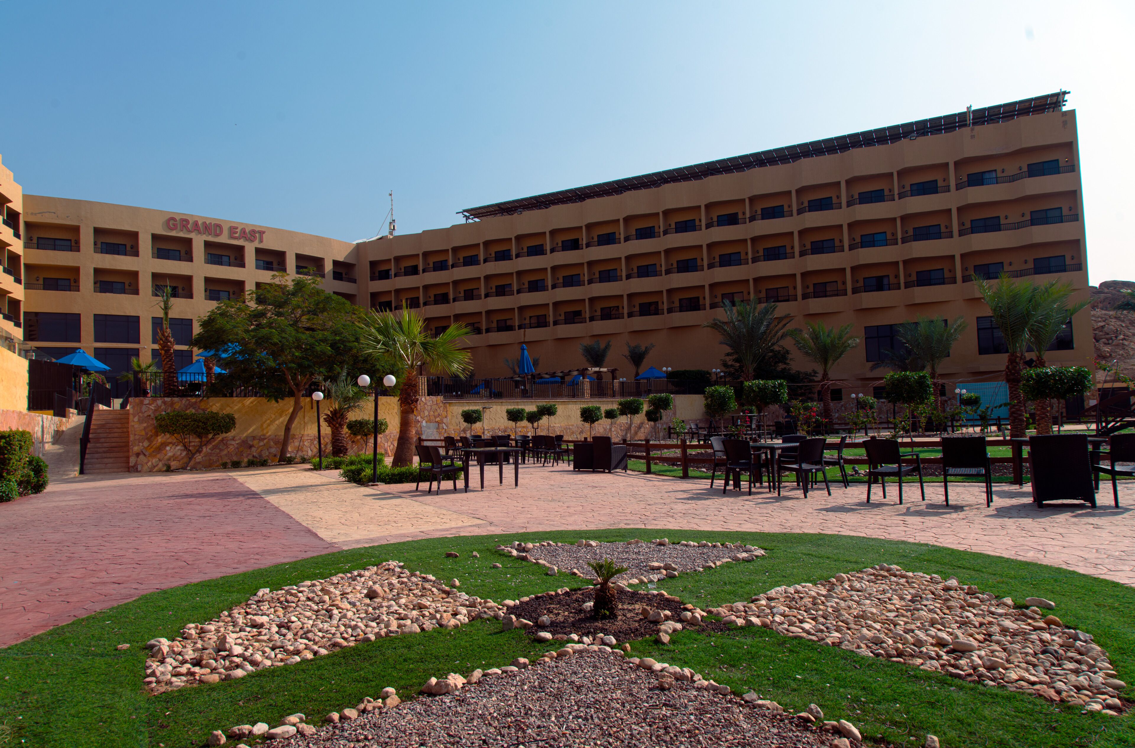Un hotel con un cortile caratterizzato da posti a sedere all'aperto, palme e un giardino curato.