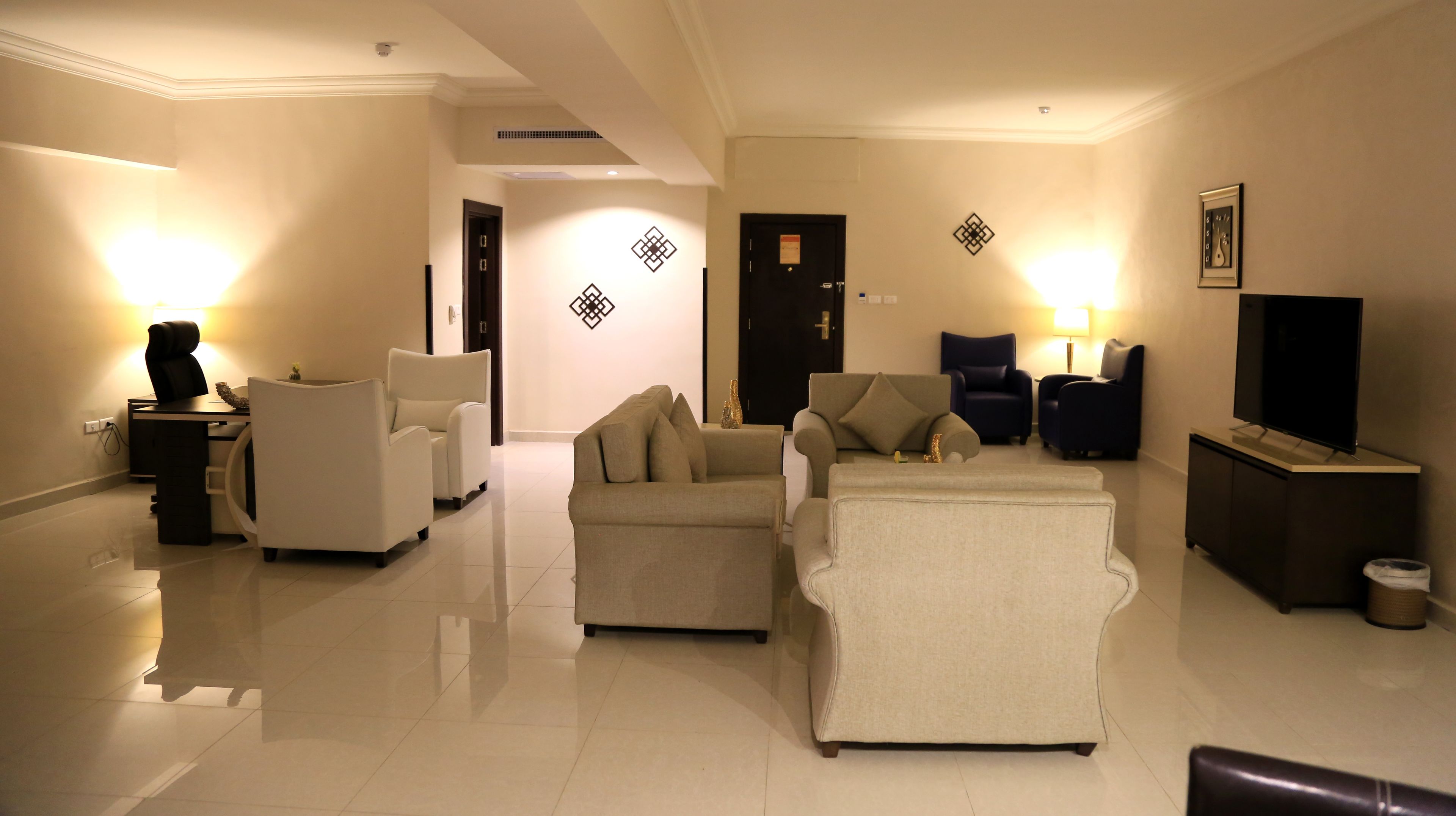 A well-lit living room with a sofa set, a TV, and a desk with a chair.