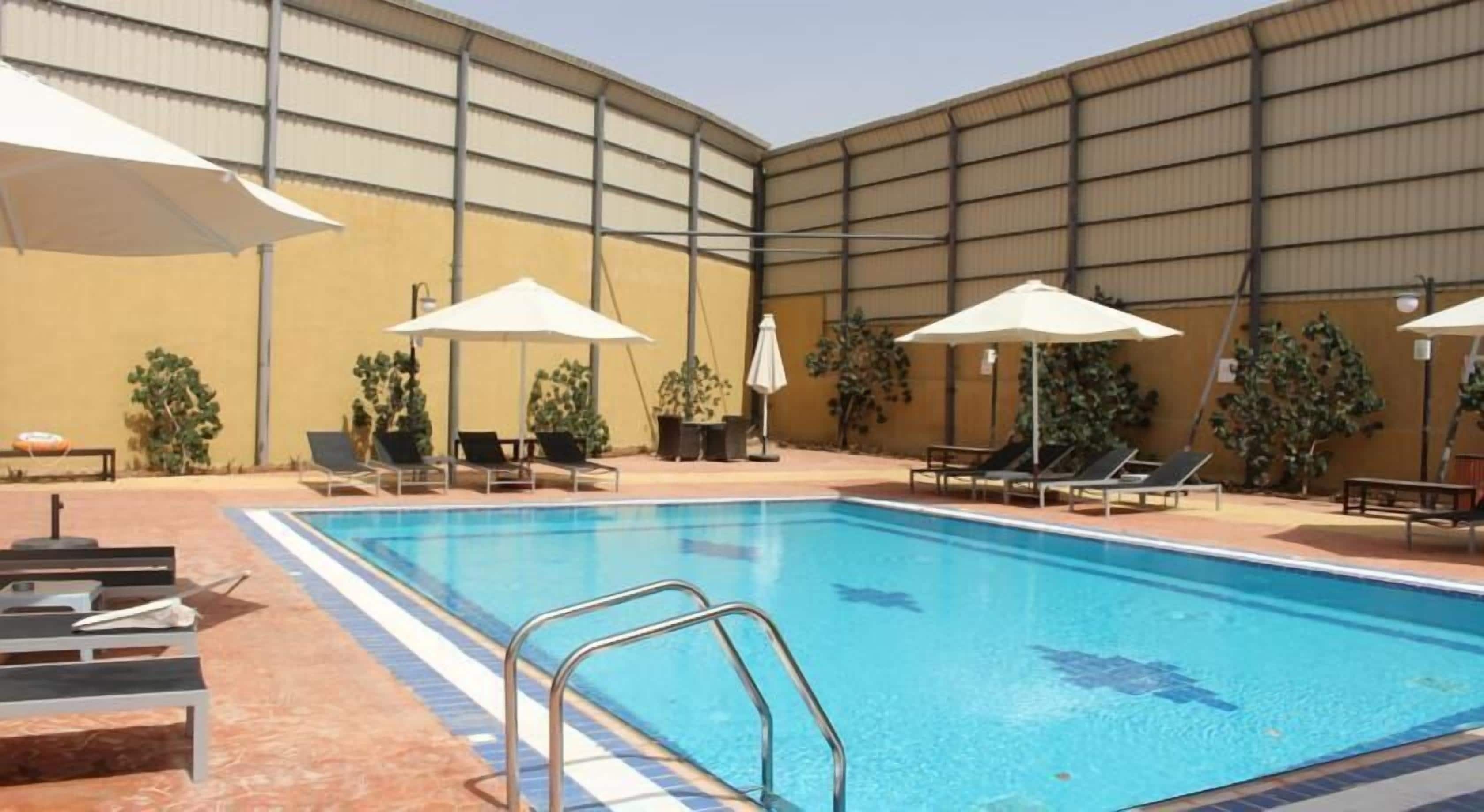 Piscina interior com espreguiçadeiras e guarda-sóis, cercada por um muro alto e plantas em vasos.