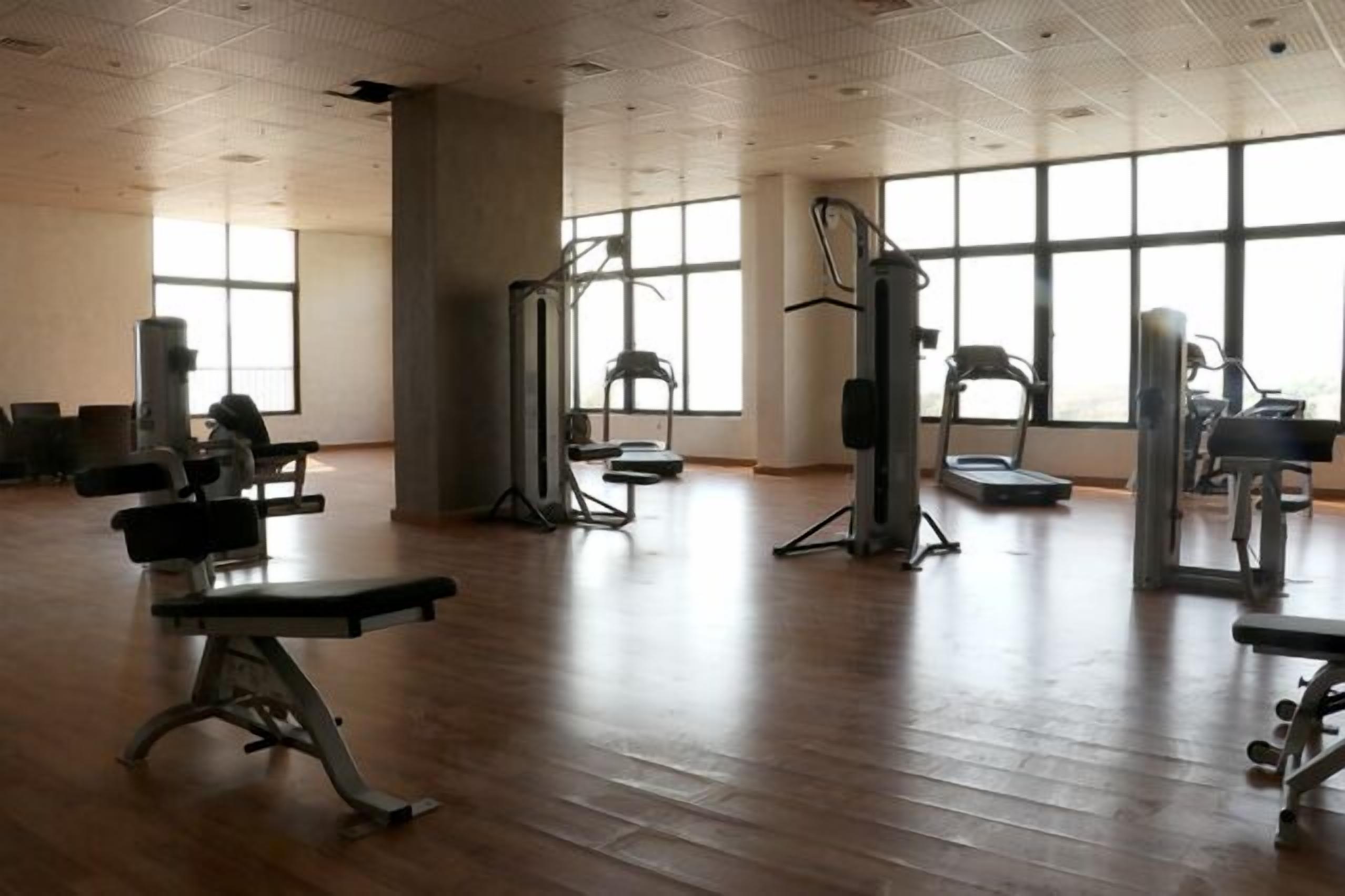 A gym with various exercise equipment, large windows, and wooden flooring.