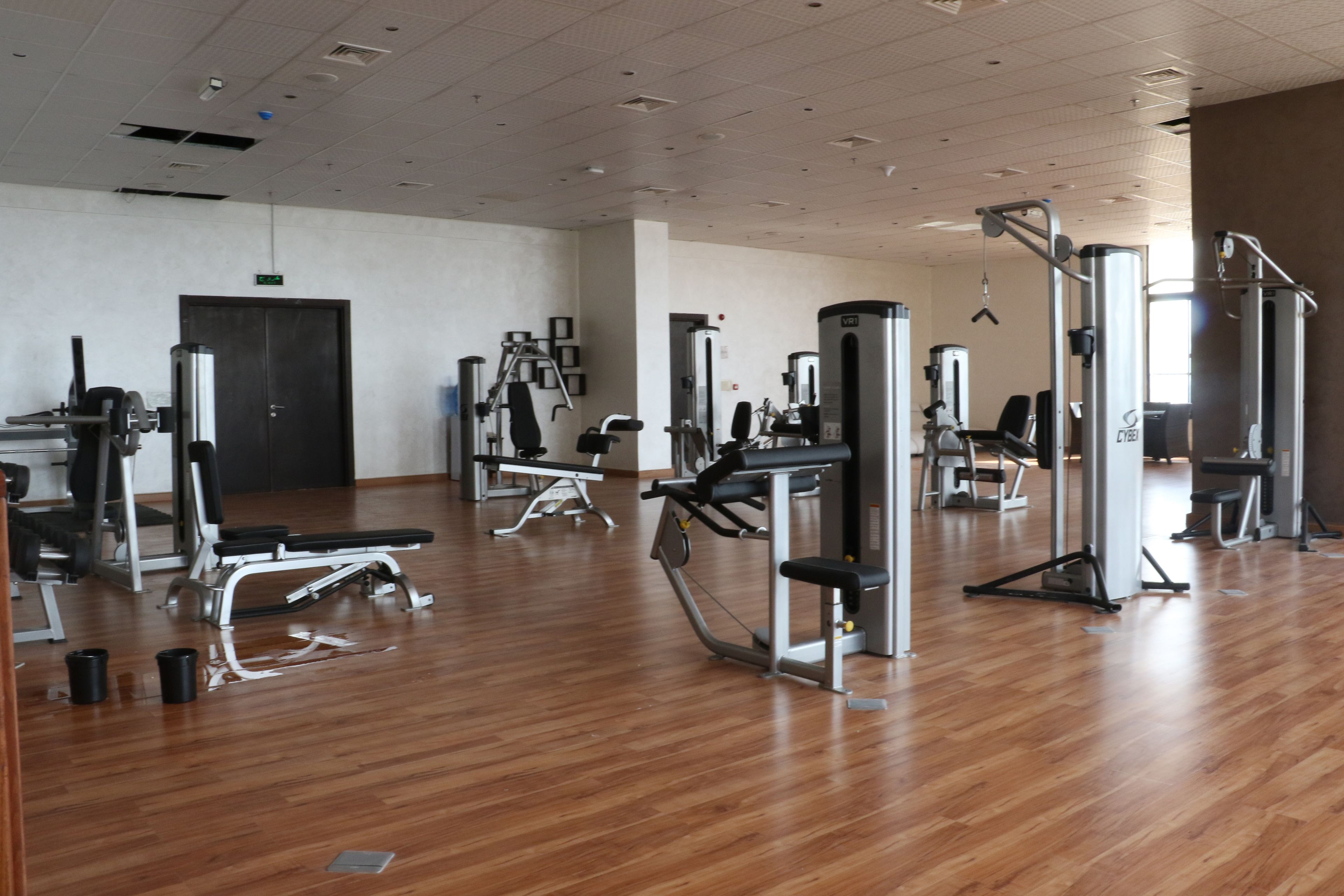 A spacious gym with various exercise machines, wooden flooring, and a door in the background.