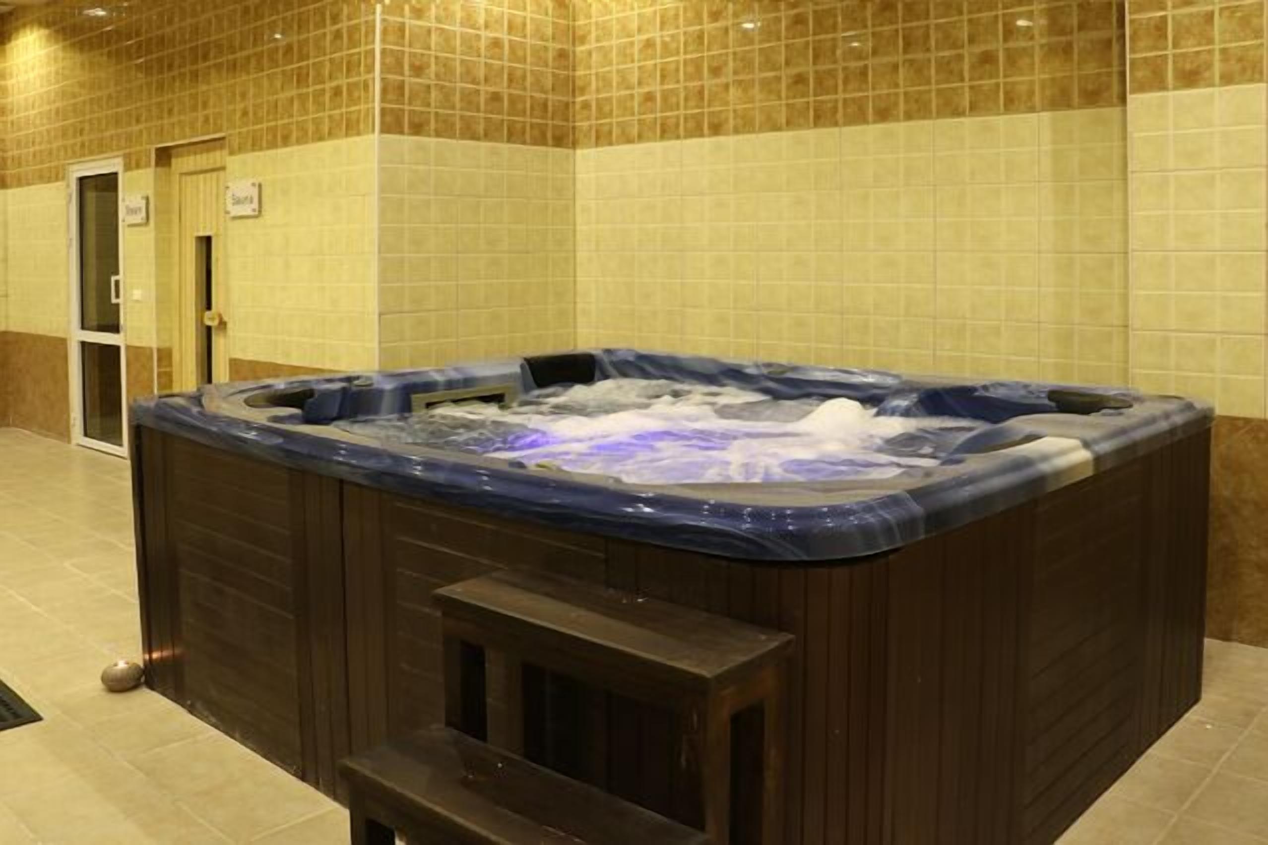 A hot tub in a room with tiled walls and a door labeled "Sauna".