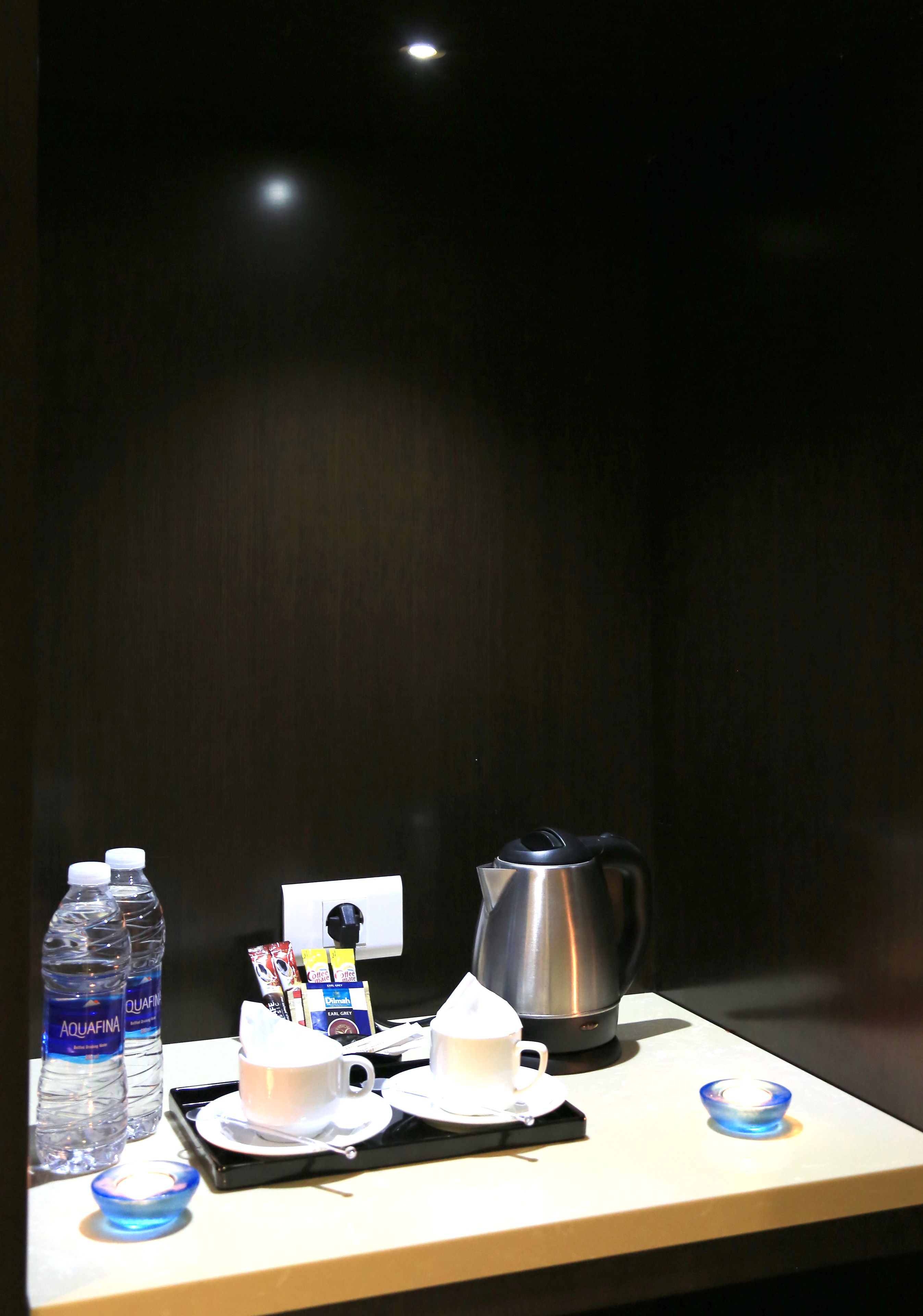 A hotel room table with a kettle, cups, saucers, a tray, and bottled water.
