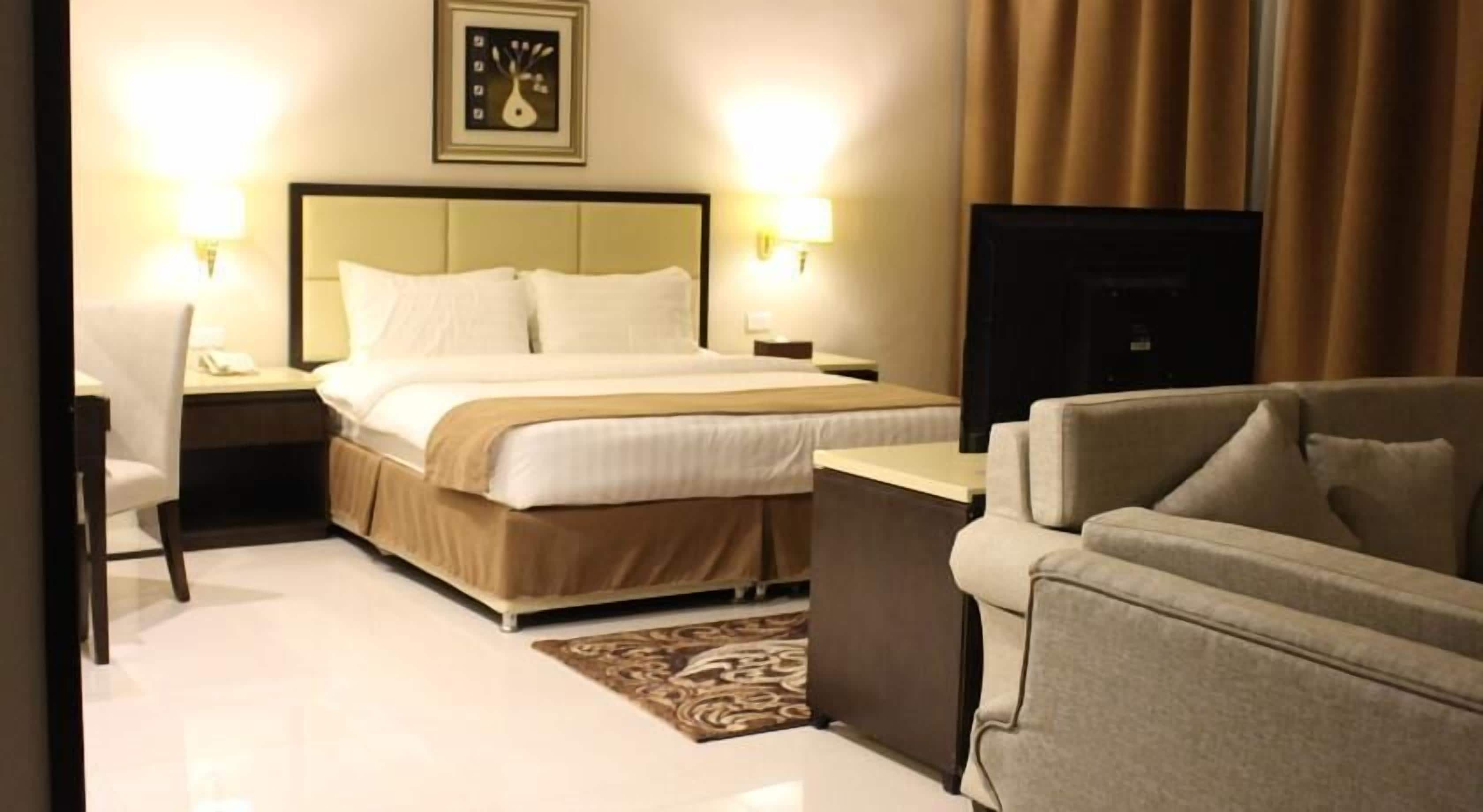 A hotel room with a bed, a desk, a chair, a television, and a wall-mounted artwork.