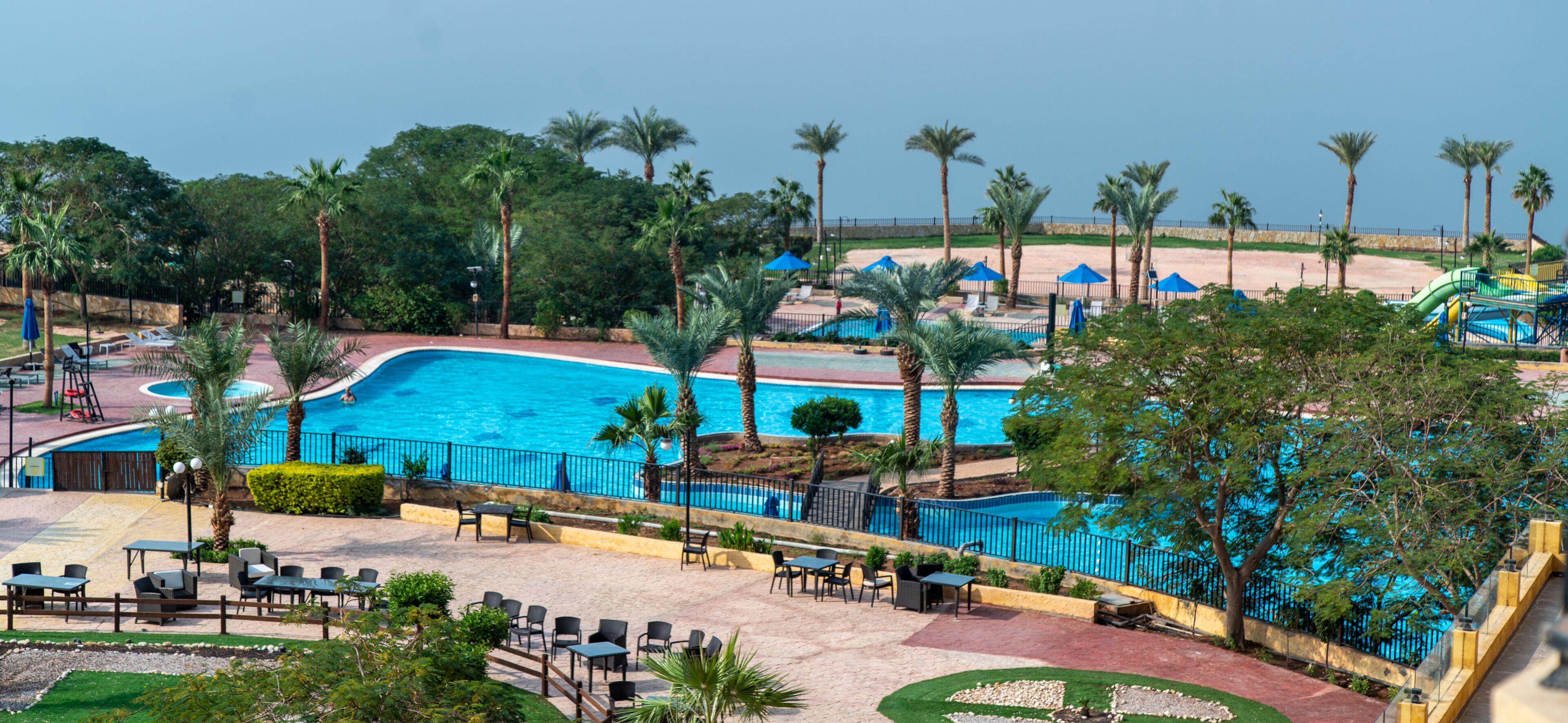 Ein Poolbereich eines Resorts mit mehreren Schwimmbecken, Palmen und Gartenmöbeln.