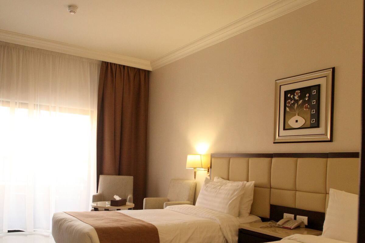 Een hotelkamer met twee bedden, een nachtkastje, een lamp en een ingelijst schilderij aan de muur.