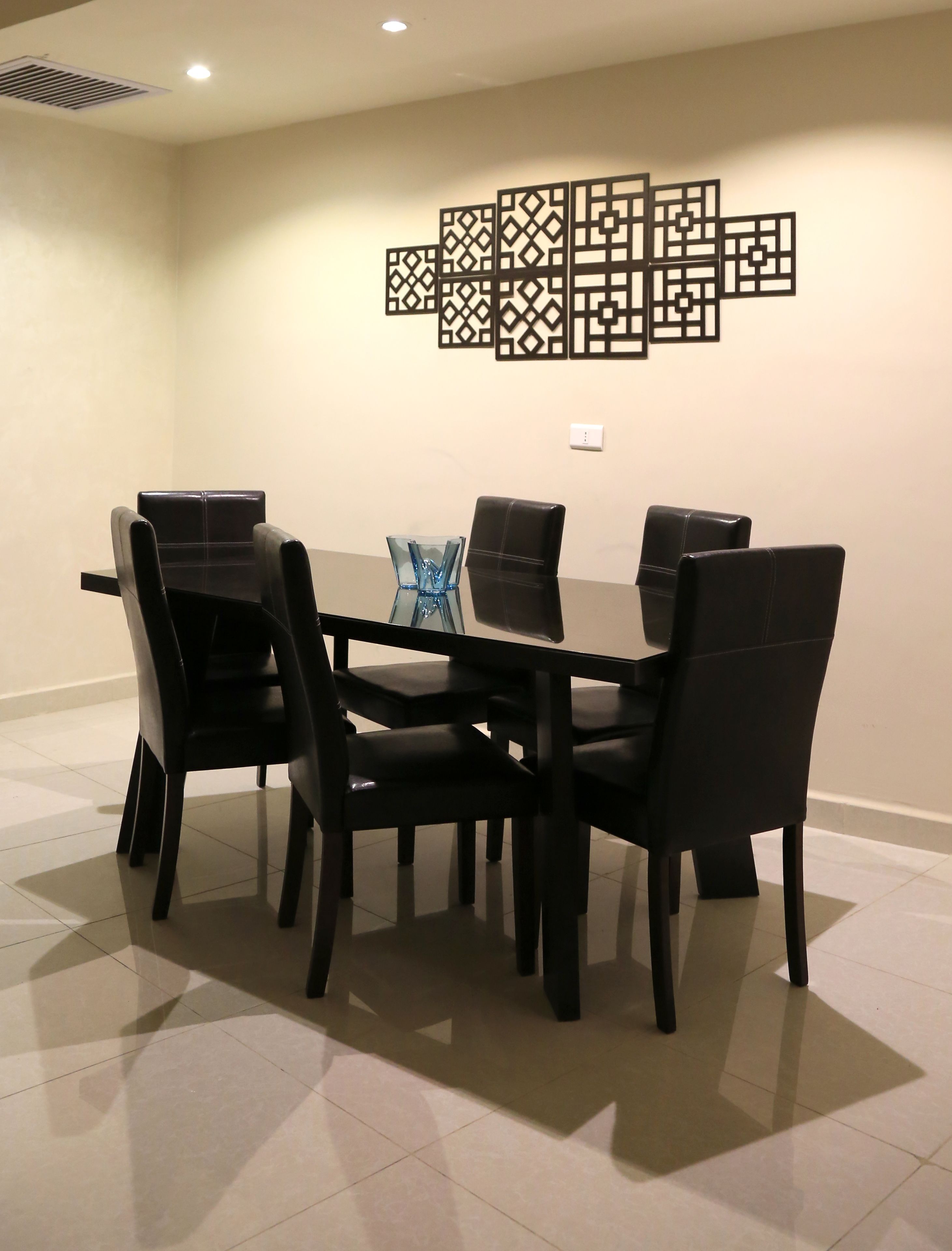 Une salle de conférence avec une table rectangulaire entourée de six chaises noires, un panneau décoratif au mur et un vase bleu posé sur la table.