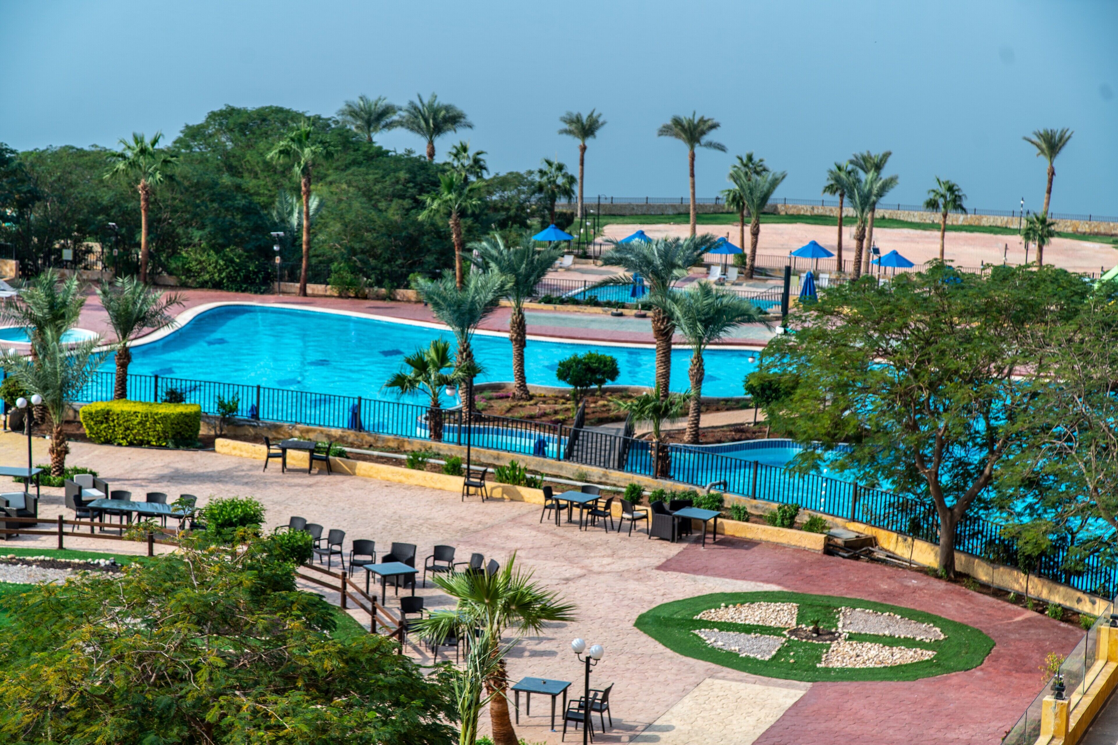 Un área de piscina en un resort con una piscina azul cristalina, rodeada de palmeras y una playa de arena.