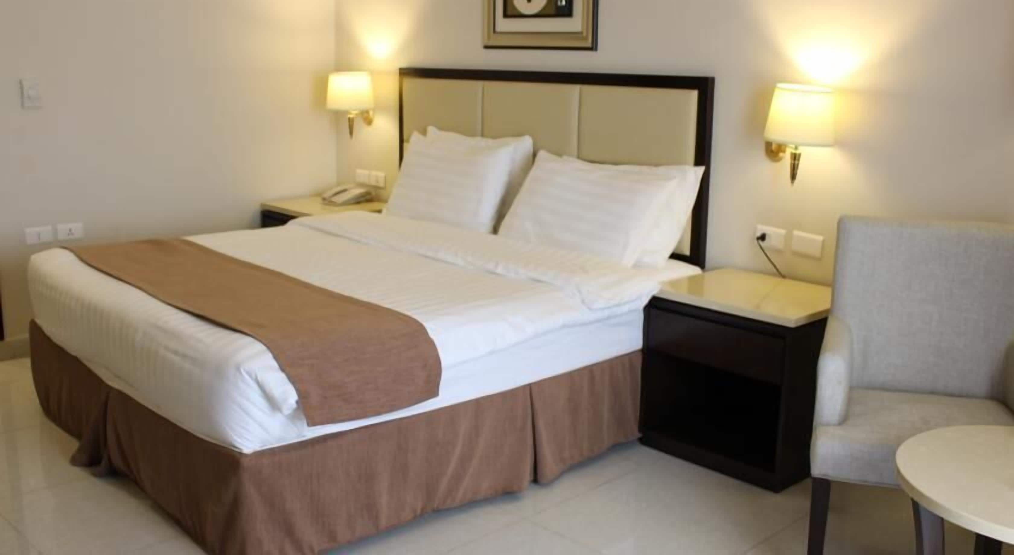 A hotel room with a large bed, two bedside tables, a chair, and wall-mounted lamps.