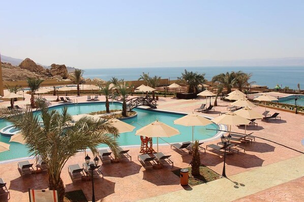 A resort pool area with multiple pools, sun loungers, umbrellas, and a view of the sea.
